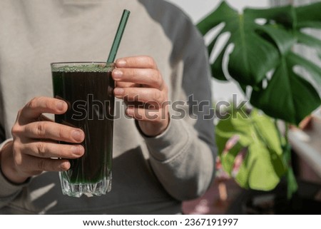 Unrecognizable woman drinking Natural organic green spirulina algae powder drink on neutral beige background. Chlorella seaweed vegan superfood cocktails smoothie supplement source and detox drinking