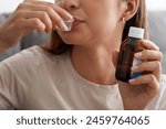 Unrecognizable woman drinks the dose of a disgusting syrup while holding the bottle of the drug in her hand