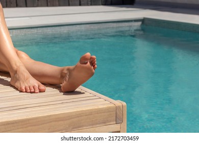 Unrecognizable woman feet laying on a sun lounger with the swimming pool in the background in hot summer time