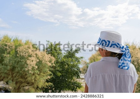 Unrecognizable woman with Greek hat enjoying a bright and beautiful summer morning from the terrace of her hotel next to a semi-wild beach on the Greek island of Crete