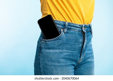 Unrecognizable woman having smartphone with empty screen in her jeans pocket on blue studio background, mockup for mobile app or website design. Space for your ad template