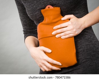 Unrecognizable woman having strong stomach ache. Female suffer on belly pain, holding hot red water bottle on abdomen. Health care, remedy for pains concept
