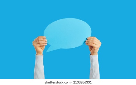 Unrecognizable woman holding empty blue speech bubble in hand on blue background. Blank paper card layout with copy space for message, quote, inspiration, opinion or vote. For advertisement