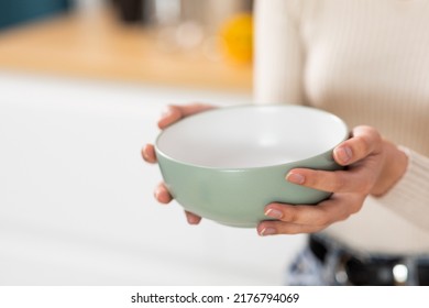 Unrecognizable Woman Holding Empty Bowl In Her Hands, Kitchen Interior, Copy Space, Closeup Shot, Cropped Of Hungry Lady Starving. Famine, Poverty, Hunger, Crisis Concept