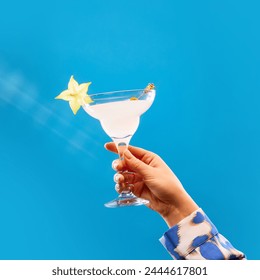 Unrecognizable woman holding glass of sweet and sour cocktail decorated with slice of carambola against blue studio background. Concept of alcohol, drink, party, degustation, holiday. Copy space. Ad - Powered by Shutterstock