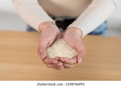 Unrecognizable Woman Holding Handful Of Rice In Her Hands, Closeup Shot. Cropped Of Lady Carrying Grain, Going To Cook Meal For Hungry Family. Crisis And Hunger, Poverty Concept