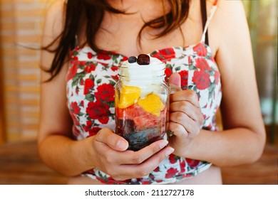 Unrecognizable Woman Holding And Showing A Jar With Chopped Fruit Salad. Mango, Apple, Grapes, Blueberries And Strawberries, With Yogurt. Vegan And Healthy Food