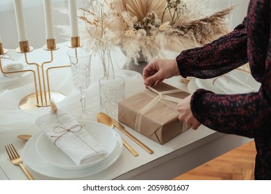 Unrecognizable Woman Hosting Elegant Dinner Party And Making Christmas Present. 

Close Up Photo Of Female Hands Setting The Table And Preparing Gifts For Christmas Dinner Party At Home.