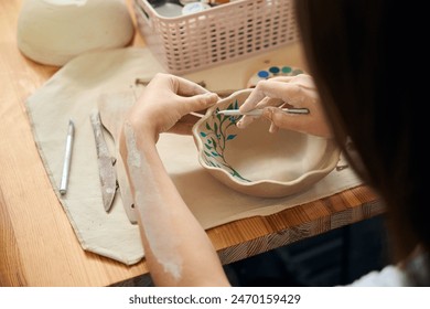 Unrecognizable woman painting clay bowl in workshop - Powered by Shutterstock