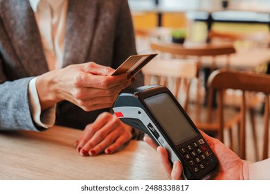 Unrecognizable woman paying the bill with a contactless credit card in a restaurant. Close up image of a female holding a creditcard and giving a payment transaction to the cashier dataphone. High - Powered by Shutterstock