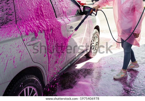 Unrecognizable woman in pink raincoat washes car at\
self-service car wash, stock\
photo