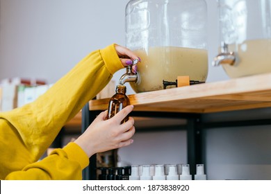 Unrecognizable woman pouring shampoo from a dispenser. Containers with natural biodegradable household chemicals in zero waste plastic free store. Dispensers for detergents, shampoo, soap, conditioner