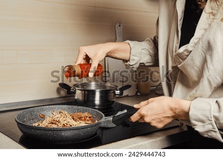 Unrecognizable woman pouring sweet chilli sauce into noodles in a frying pan