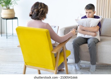 Unrecognizable woman psychotherapist conducts therapy with teenager. School psychologist. Frustrated boy hugs pillow to himself.