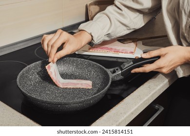 Unrecognizable woman put bacon on hot frying pan in the kitchen - Powered by Shutterstock