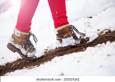 Unrecognizable woman in red trousers and leather boots outside in snow.