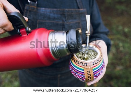 unrecognizable woman serving mate with a red thermo, in a colorful ethnic mate.