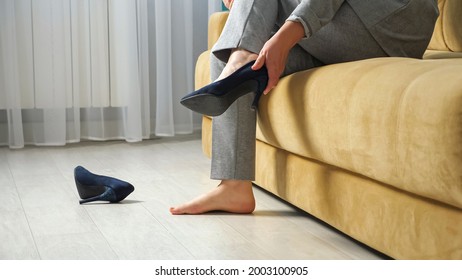 Unrecognizable Woman Sits On The Sofa And Takes Off High Heel Shoes.