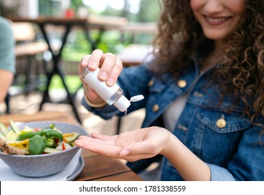 Unrecognizable woman sitting outdoors on terrace restaurant, disinfecting hands.