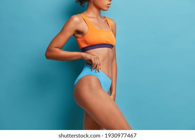 Unrecognizable Woman Stands In Profile Indoor Against Blue Background Has Perfect Slim Body Has Healthy Skin. Example Of Sport Or Fitness Surgery