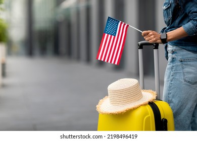 Unrecognizable woman with straw hat on yellow suitcase holding flag of the US, posing in airport, panorama with copy space. Travelling, tourism, vacation, holidays, education abroad concept