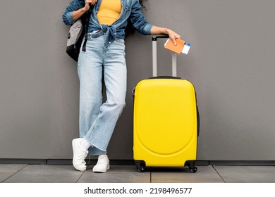 Mujer irreconocible con elegante viajero casual vestido de pie sobre fondo gris, llevando equipaje amarillo y mochila, con pasaporte y boletos de avión, recortado, espacio para copiar