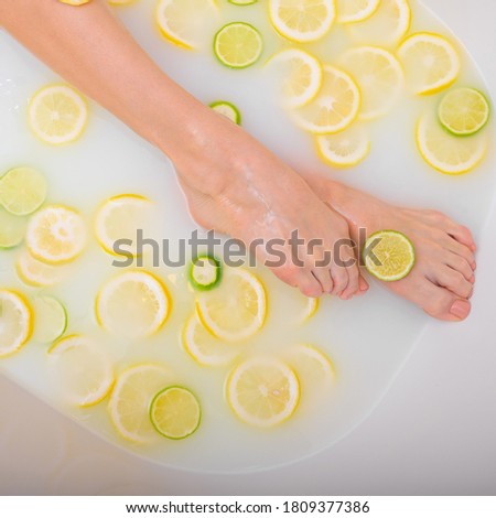 Unrecognizable woman takes a milk bath with lemons and limes. Citrus spa. Body care. Skin whitening. Female legs top view.