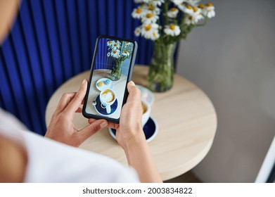 Unrecognizable Woman Taking A Food Photography Of Served Table With Macarons And Cup Of Coffee Latte Or Cappuccino In Stylish Coffee House. Mobile Phone In Live View Mode. Still Life