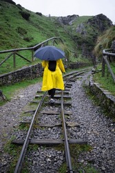 Unerkennbare Frau Mit Regenschirm Und Gelbem Regenmantel An Einem Regnerischen Tag, Die Auf Den Spuren Eines Alten Bergbauzuges In Den Covadonga Seen Spaziert. Asturien - Spanien