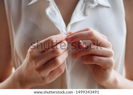 Unrecognizable woman unbuttoning white blouse at home. Close-up view on hands [[stock_photo]] © 