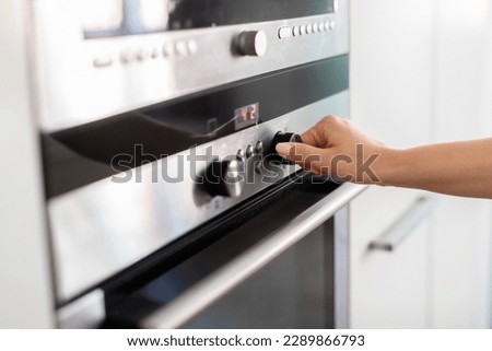 Unrecognizable Woman Using Electic Oven In Kitchen, Adjusting Temperature With Hand, Young Housewife Turning Knob, Selecting Burner Cooking Mode While Preparing Food At Home, Closeup Shot