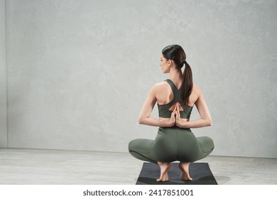 Unrecognizable woman wearing green gym clothes sitting back in yoga asana, with hands in namaste gesture behind back on gray background with studio light. Mindfulness and mental health concept. - Powered by Shutterstock