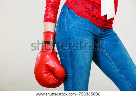 Unrecognizable woman wearing red boxing glove, and tight blue jeans. Grey background.