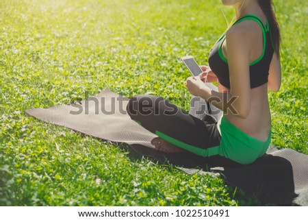 Unrecognizable woman wearing sportswear listening to music during training outdoors while sitting on the mat. Stretching, wellness, calmness, relax, healthy, active lifestyle concept