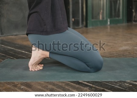 Unrecognizable woman yogi and new teacher doing a kneeling pose with tucked toes, workout yoga training, barefoot and wearing sportswear, green yoga mat on wooden floor, close-up side view photo
