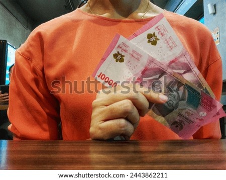 Unrecognizable woman's hand holding two hundred thousand Indonesian rupiah banknotes in one hundred thousand denomination. Cash management concept.