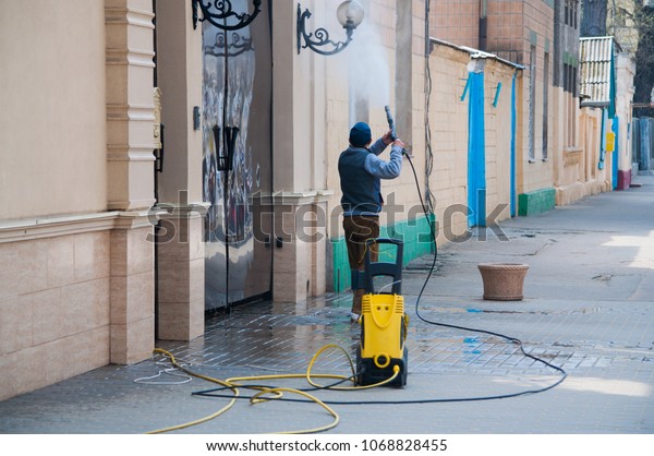 An\
unrecognizable worker cleaning the building with high pressure\
washing machine. Water stream washing the\
wall