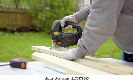 unrecognizable worker in nature sawing board with electric jigsaw. concept of working in country house on street, building fence or building from wooden boards. Jigsaw at work