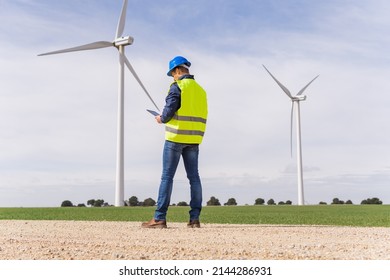 Unrecognizable Worker From The Renewable Energy Sector, From The Back Looking At His Digital Tablet In A Field Of Wind Turbines. Increase In Energy Prices In The Market And Alternative Energies.