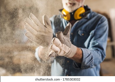 Unrecognizable workingman with work gloves on clapping to remove sawdust