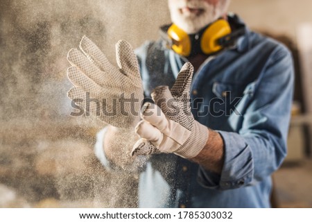 Unrecognizable workingman with work gloves on clapping to remove sawdust