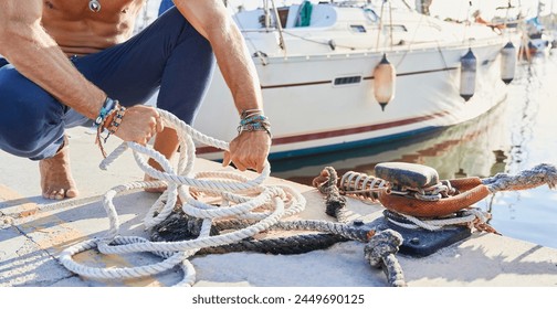 Unrecognizable young adult man tying up a mooring rope at the dock of the yacht marina before setting off to sail - Powered by Shutterstock