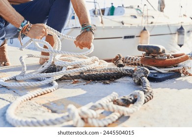 Unrecognizable young adult picks up a mooring rope from the ground at the marina dock to set off sailing his sailboat - Powered by Shutterstock