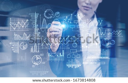 Unrecognizable young businesswoman drawing graphs on glass board in blurry office. Concept of investment and market analysis. Toned image double exposure