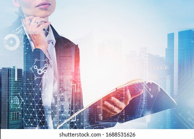 Unrecognizable Young Businesswoman Standing With Notebook In Abstract City With Double Exposure Of Blurry Internet Interface And Hi Tech Icons. Concept Of Technology. Toned Image