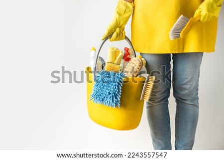 Unrecognizable young caucasian woman in a uniform wearing yellow rubber gloves and holding bucket full of cleaning supplies. Cleaning company service advertisement. House cleaning concept