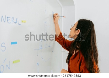 Unrecognizable young economics teacher writes on blackboard with graphs