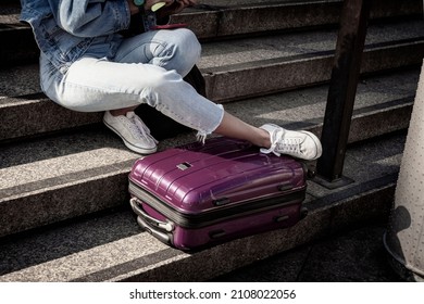 Unrecognizable young girl student sitting resting on the steps with a suitcase, summer sunny day, youth travel and tourism concept