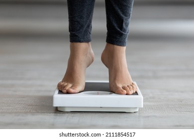 Unrecognizable young Indian lady checking her weight, standing on scales indoors, closeup of feet. Cropped view of millennial woman on diet, leading healthy lifestyle, losing excess kilos