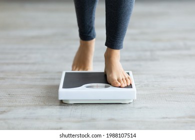 Unrecognizable young Indian woman stepping on scales to measure her weight at home, closeup of feet. Cropped view of millennial lady checking result of her slimming diet. Healthy living concept - Shutterstock ID 1988107514